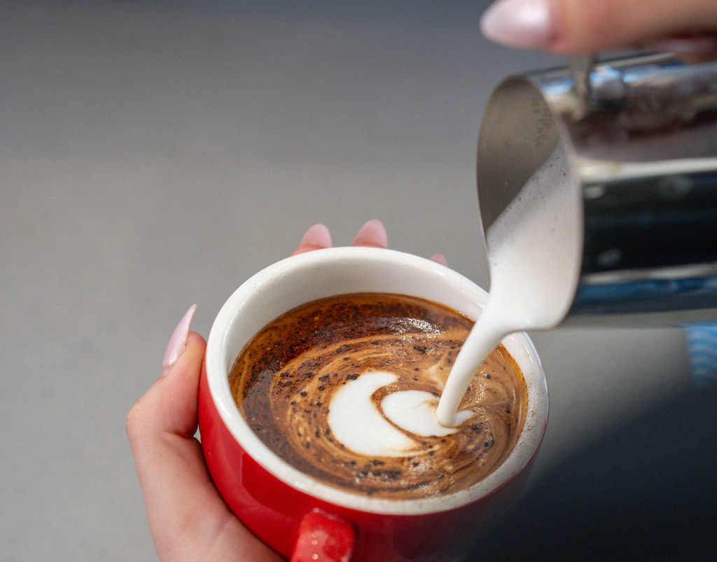 Barista pouring latte art into a red cup